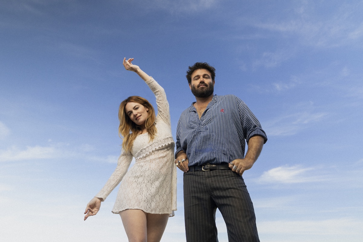 Promotional portrait of Australian folk-pop duo Angus & Julia Stone standing outdoors against a bright blue sky.